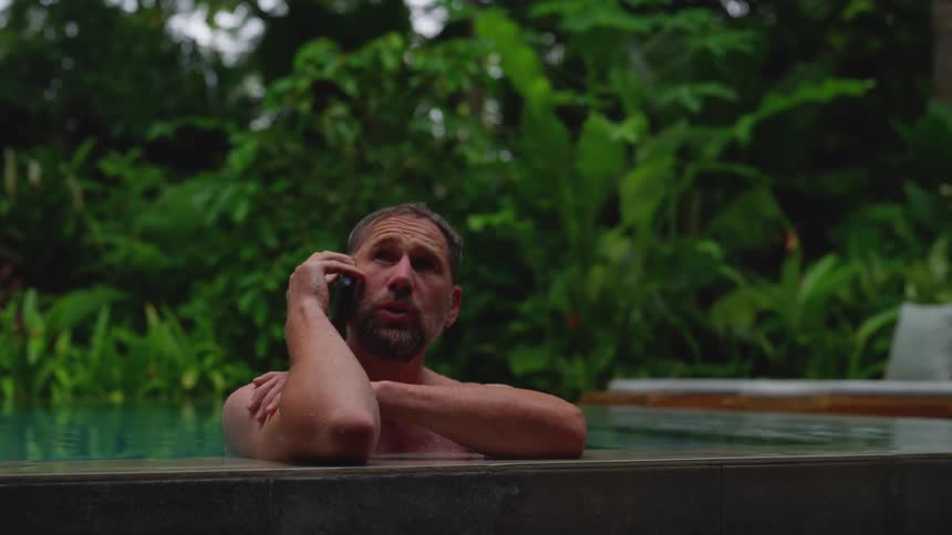 Man takes a phone call while relaxing in a tropical pool