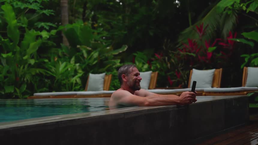 Man in the pool at tropical resort spa interacting with a smartphone