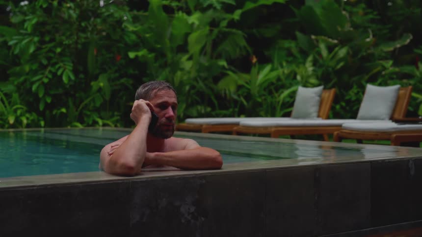Male leaning on edge of infiniti pool talking on a cell phone