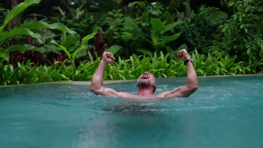 A man joyfully jumps into a pool enjoying his vacation