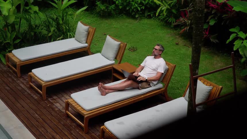A man uses a laptop while sitting on an outdoor lounge chair during daytime