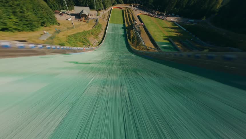 FPV Aerial Flying Low Over a Sunlit Olympic Ski Jump Ramp in Sunny Weather