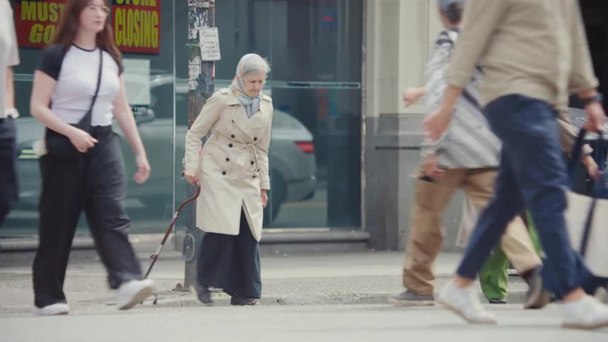 Elderly woman walks along a busy city street during daytime