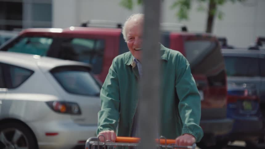 Happy elderly man pushing a shopping cart across the parking lot