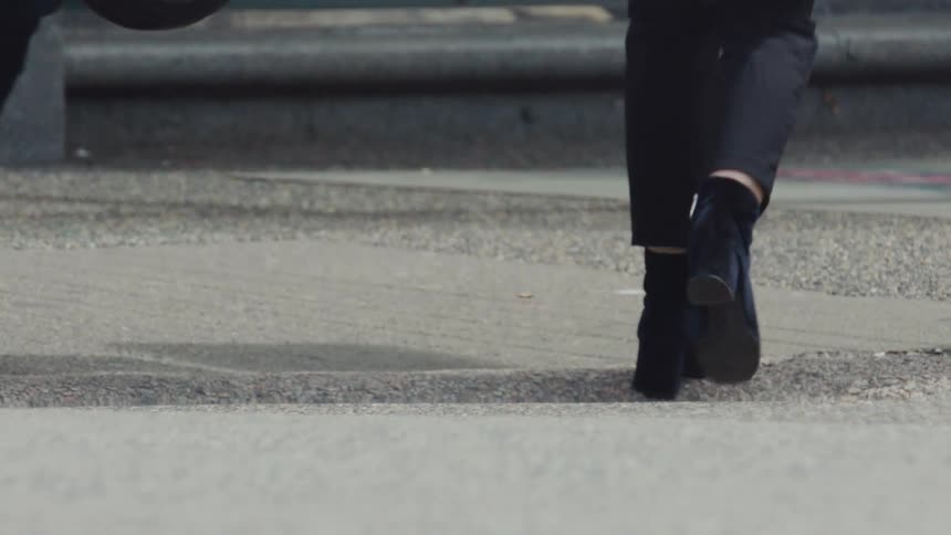 Close up of a womans legs and footwear as she walks through a busy street during daytime