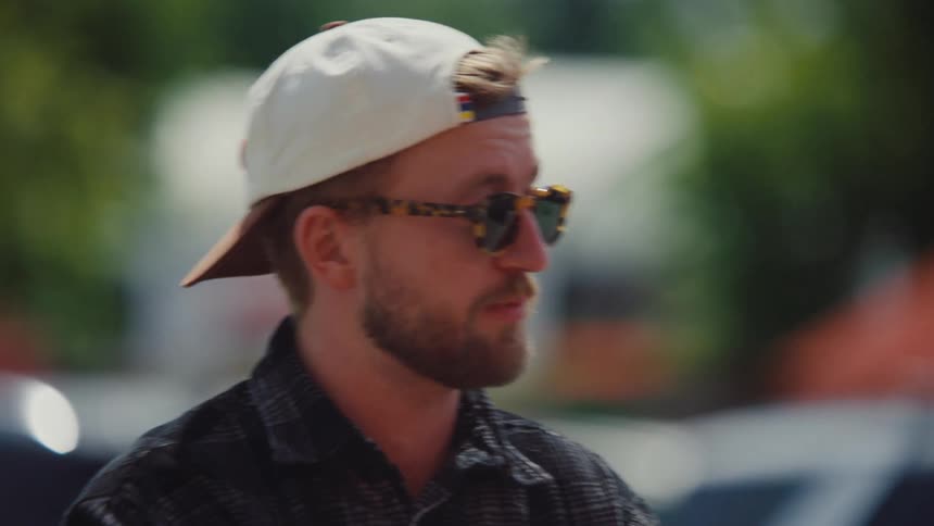 Man in cap and glasses walking with a shopping cart through the parking lot