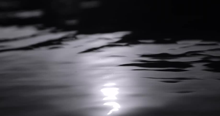 The video shows a dark reflective surface likely water with a single bright light source shimmering on its surface the light creates a distorted elongated reflection suggesting movement on the waters surface