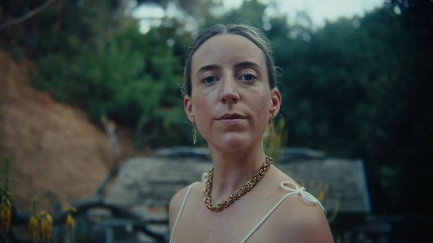 The face of a woman with her hair tied up wearing a necklace around her neck and looking forward while moving her head