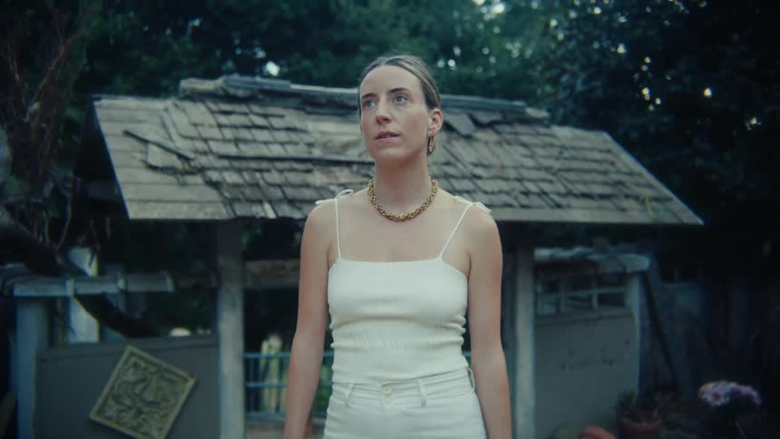 An unbothered female in a white outfit standing in front of a shed