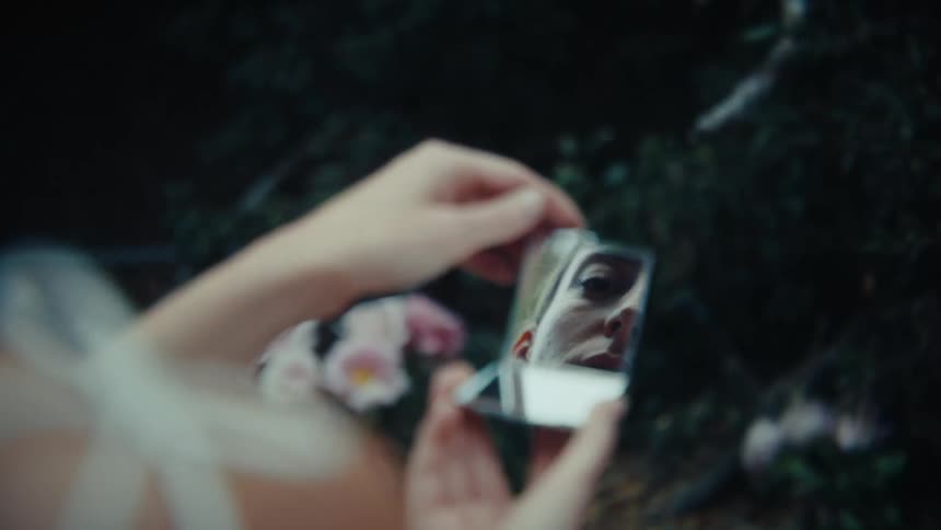 A woman looks at herself in a small mirror
