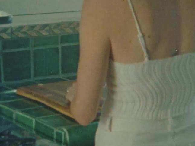 A young woman wearing a white dress cutting a lemon on a cutting board in the kitchen with a knife