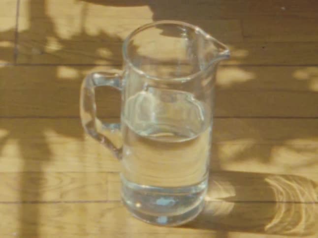 Person picks up a glass pitcher holding water from the wooden floor