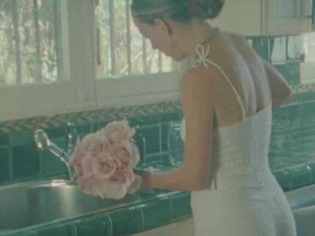 A person with a bun and a necklace holds a bouquet of pink roses over a kitchen sink preparing them under bright diffused light