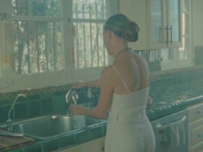A woman fills a cup with water from the kitchen sink