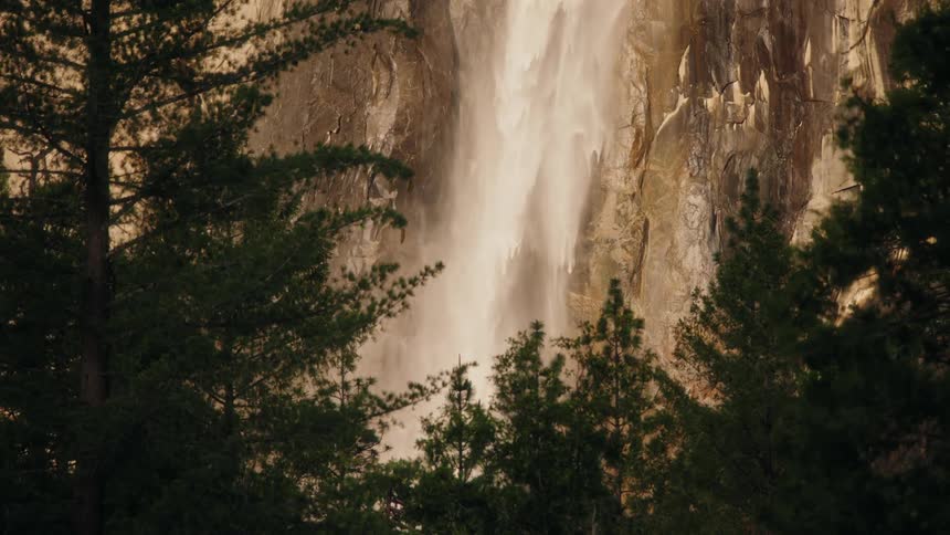 Waterfall travels down the craggy mountainside in front of a thick forest