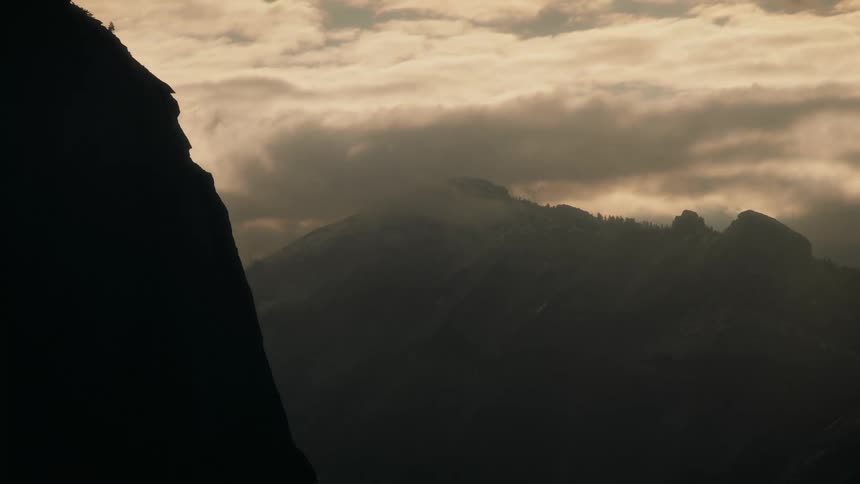 Heavy clouds dim the sunlight falling onto foggy mountains