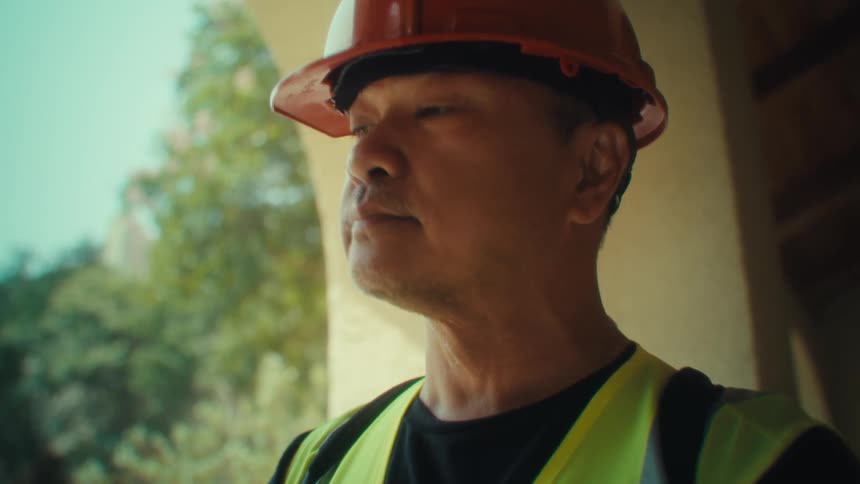 A person in a red hard hat and highvisibility vest holds a tablet in front of a house surrounded by greenery
