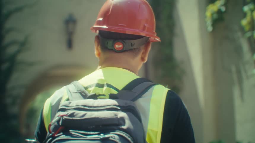 Worker with red protective helmet and backpack walking in an outdoor environment