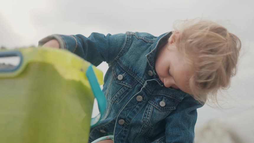 Blonde girl with jeans jacket playing with sand in the beach