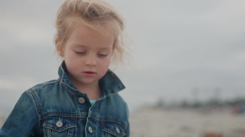 A young child with lightcolored hair wearing a denim jacket is shown in a closeup shot their gaze is directed downwards suggesting they are focused on something just out of frame or lost in thought