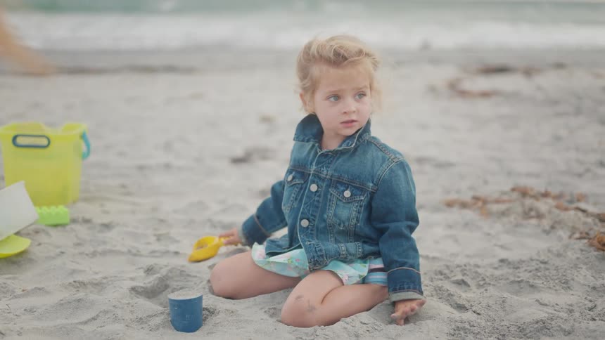 A child wearing a jean shirt playing with sand on the beach at midday
