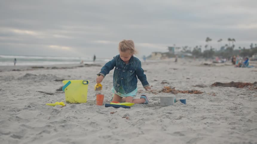 A child packing sand into a cup with a bucket beside her on the beach at midday