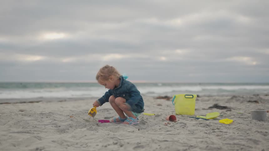 Little girl having fun playing with sand on the beach