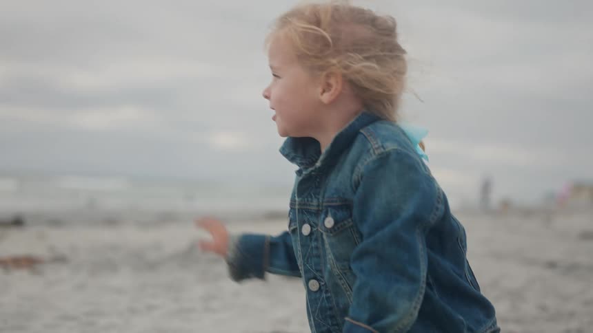 The child is walking and waving on the beach