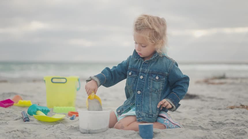 Little girl filling a bucket with sand while playing on the beach