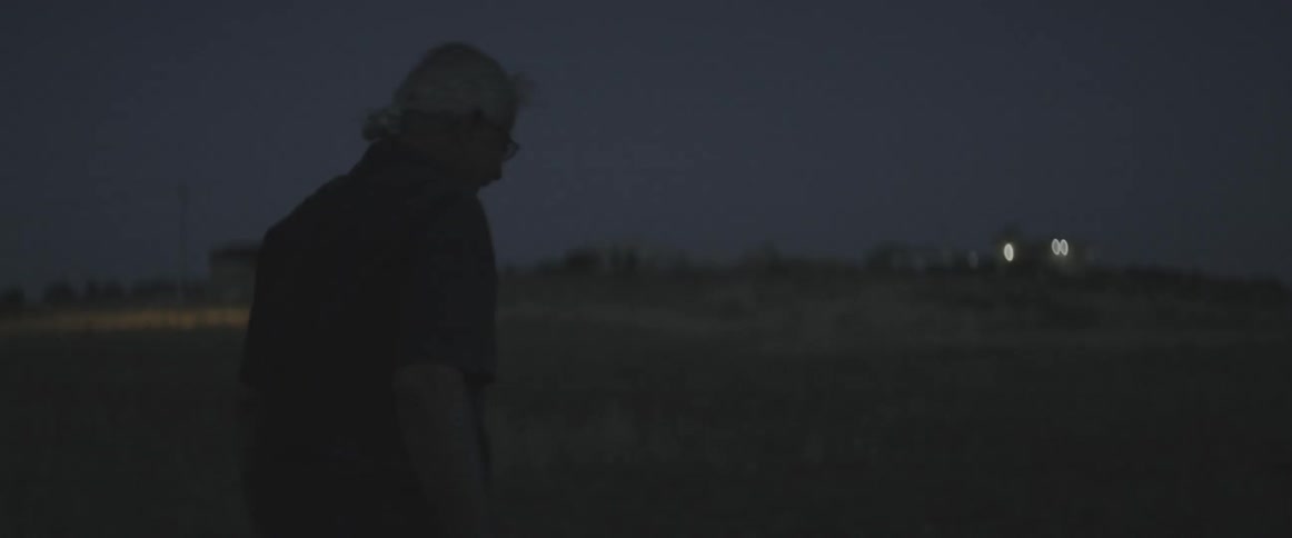 A man walks outdoors in an open field at night
