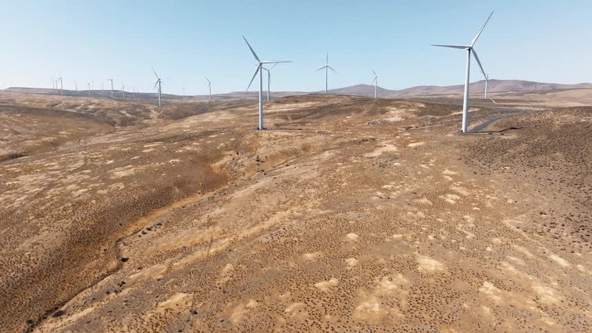 A windmill with a series of turbine blades turning clockwise in a field at midday