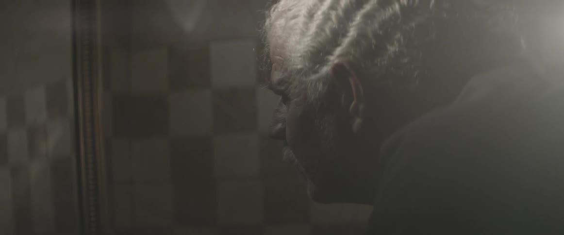 An elderly man looks into a bathroom mirror