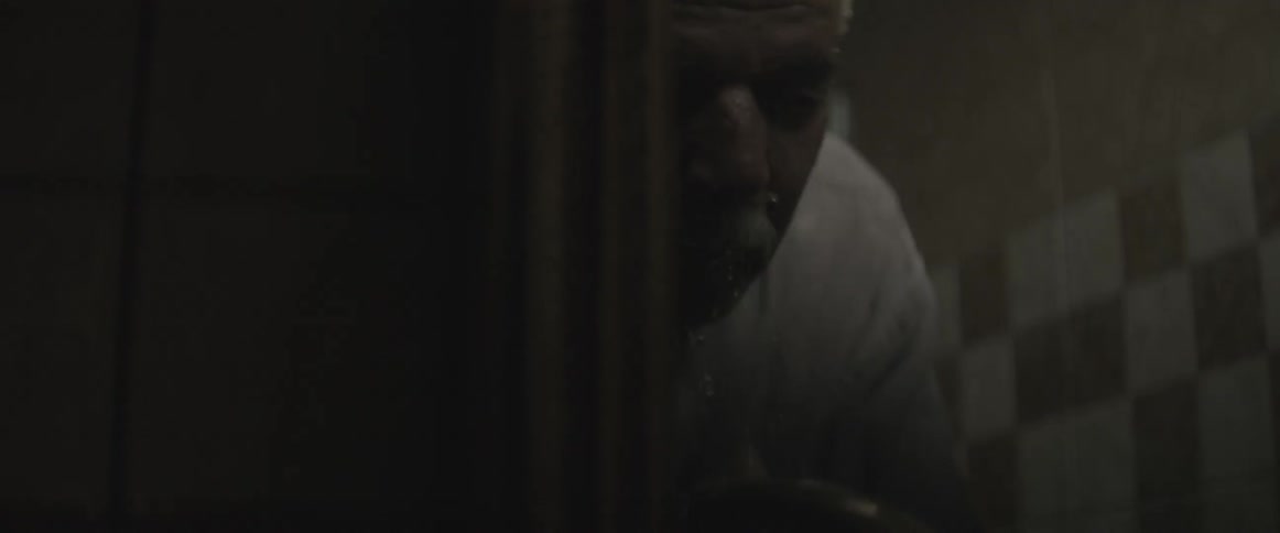 A man splashes water on his face and looks into a bathroom mirror