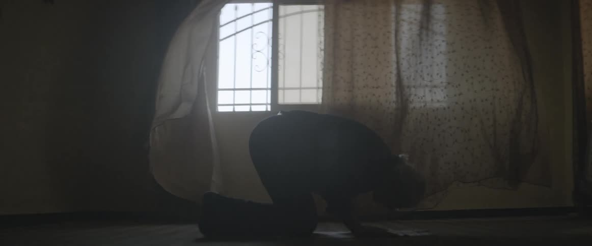 A man kneels to pray in front of billowing curtains