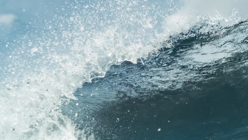 Breaking wave sprays water drops into the air on a cloudy day before obscuring the sky