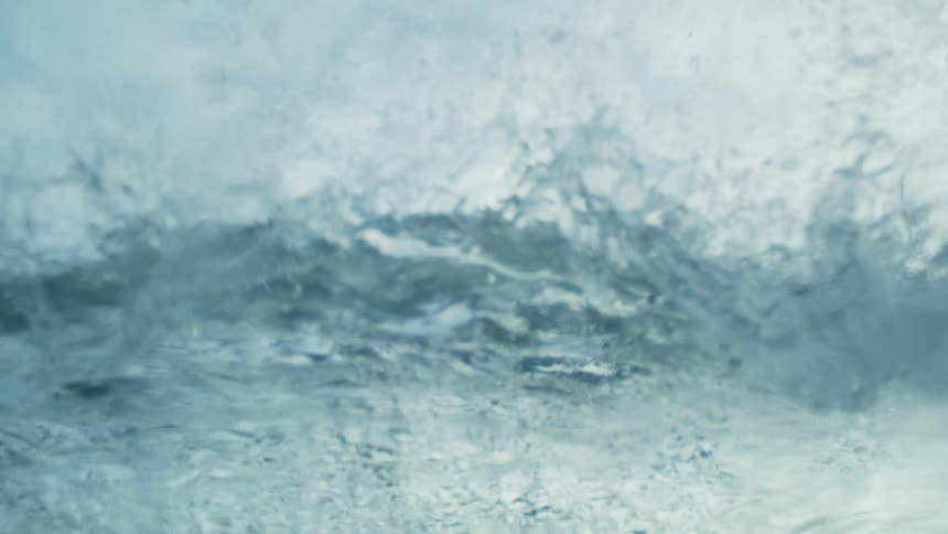 A gentle wave crests under a cloudy sky in the open ocean