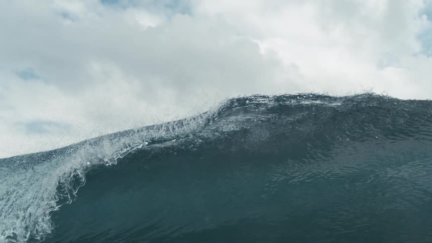 The video captures a powerful ocean wave as it rises and crests showing the intricate details of the breaking water and foam the cloudy sky in the background suggests an overcast day emphasizing the raw power of the ocean