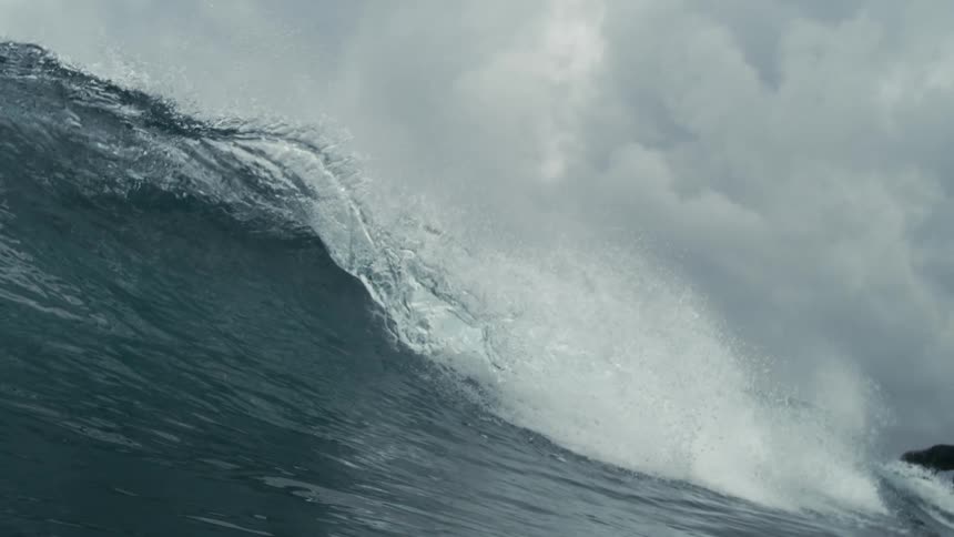 A powerful ocean wave with a foamy crest is captured under a dark cloudy sky