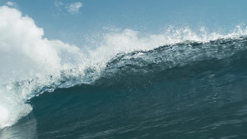 A gentle wave rolls across the ocean under a cloudy blue sky