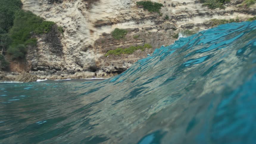 Clear ocean wave rises near rocky coastal cliff