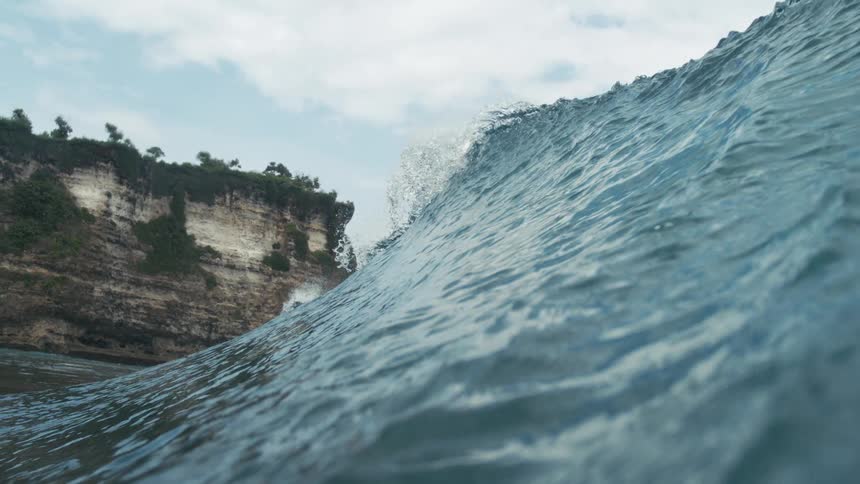 A large ocean wave rises near rocky coastal cliffs