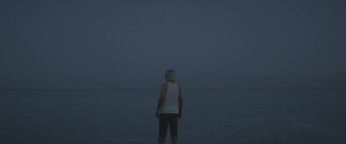Man standing in shallow ocean waters at dusk