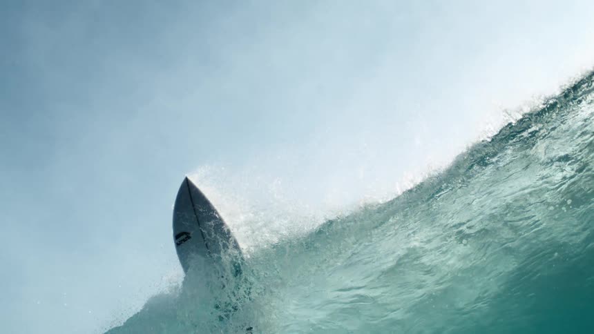 Wave swells beneath an abandoned surfboard then breaks on a sunny day