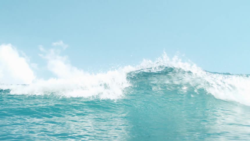 A vibrant blue ocean wave crests and undulates under a bright sky with white clouds