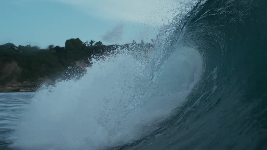 Large ocean wave crashing powerfully near shore with water spraying dramatically against a cloudy backdrop