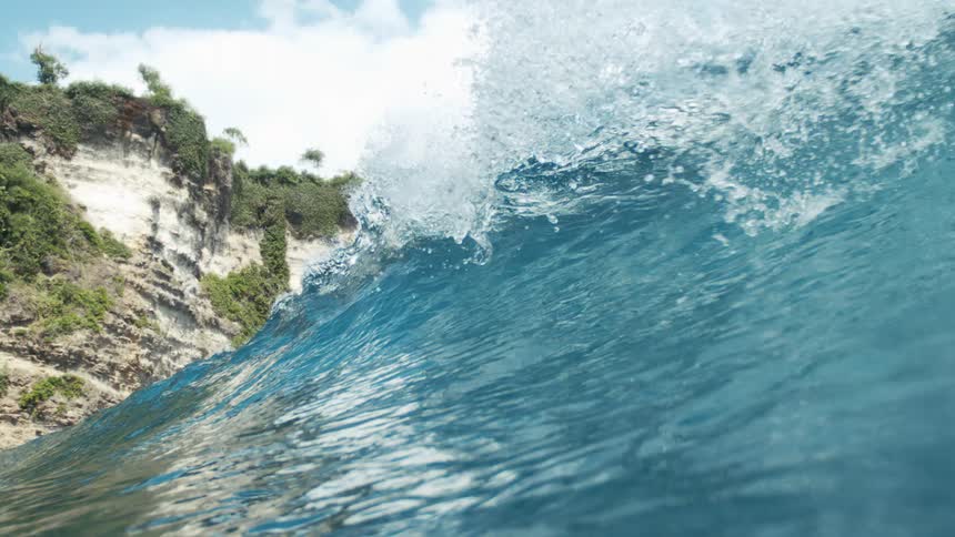 A wave forms and crashes along the ocean surface outdoors during daytime