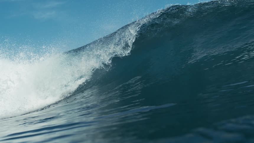A powerful ocean wave curls under a clear blue sky