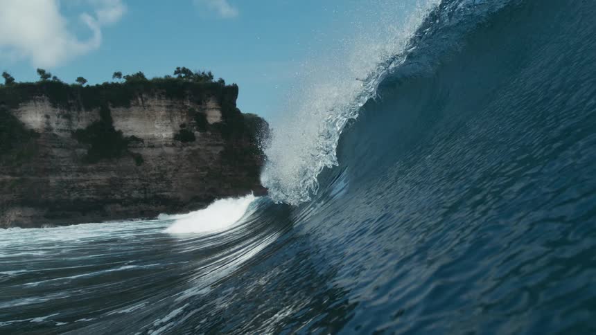 A huge wave forms and crashes on the ocean surface during daytime