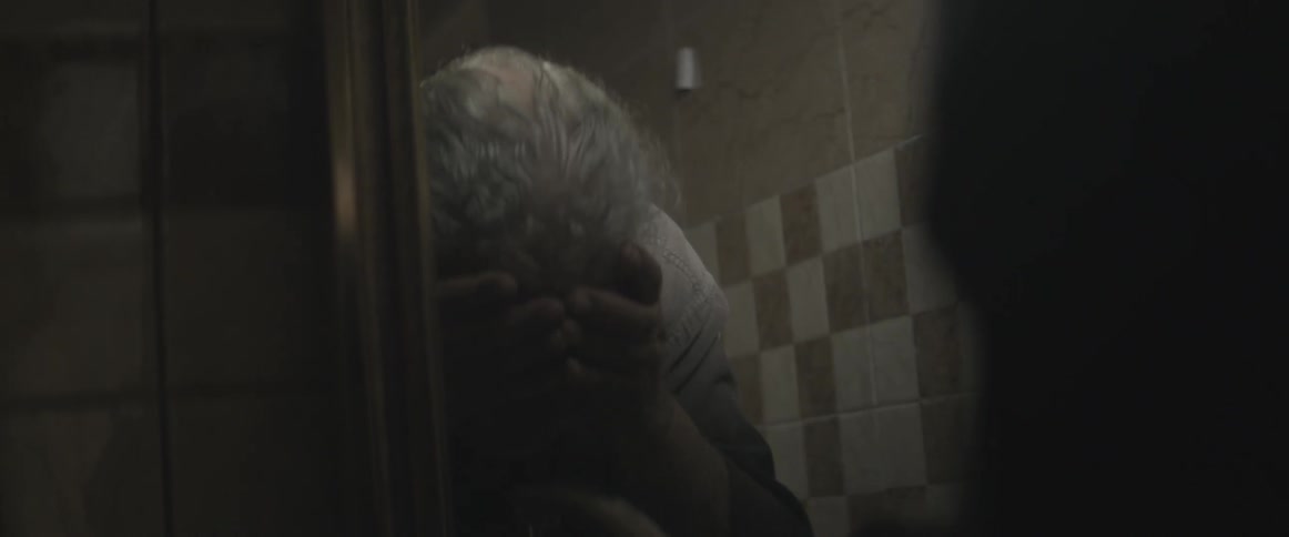 An elderly man washes his face and looks at his reflection