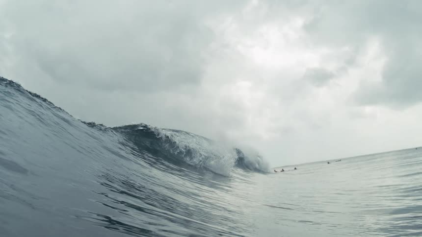 A powerful ocean wave with a breaking crest under a dramatic cloudy sky with hints of other waves